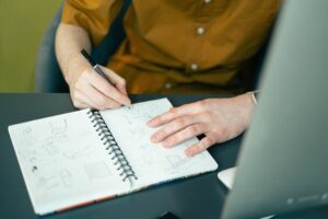 Close-up of a designer sketching ideas in a spiral notebook at a desk, highlighting creativity.