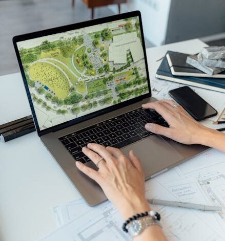Architect working on landscape plan displayed on laptop with hands typing on keyboard.